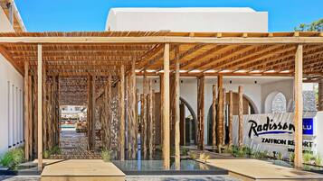 Un espacio al aire libre cubierto con vigas de madera y una piscina, que conduce a un edificio con un letrero que dice "Radisson Zafron Resort".