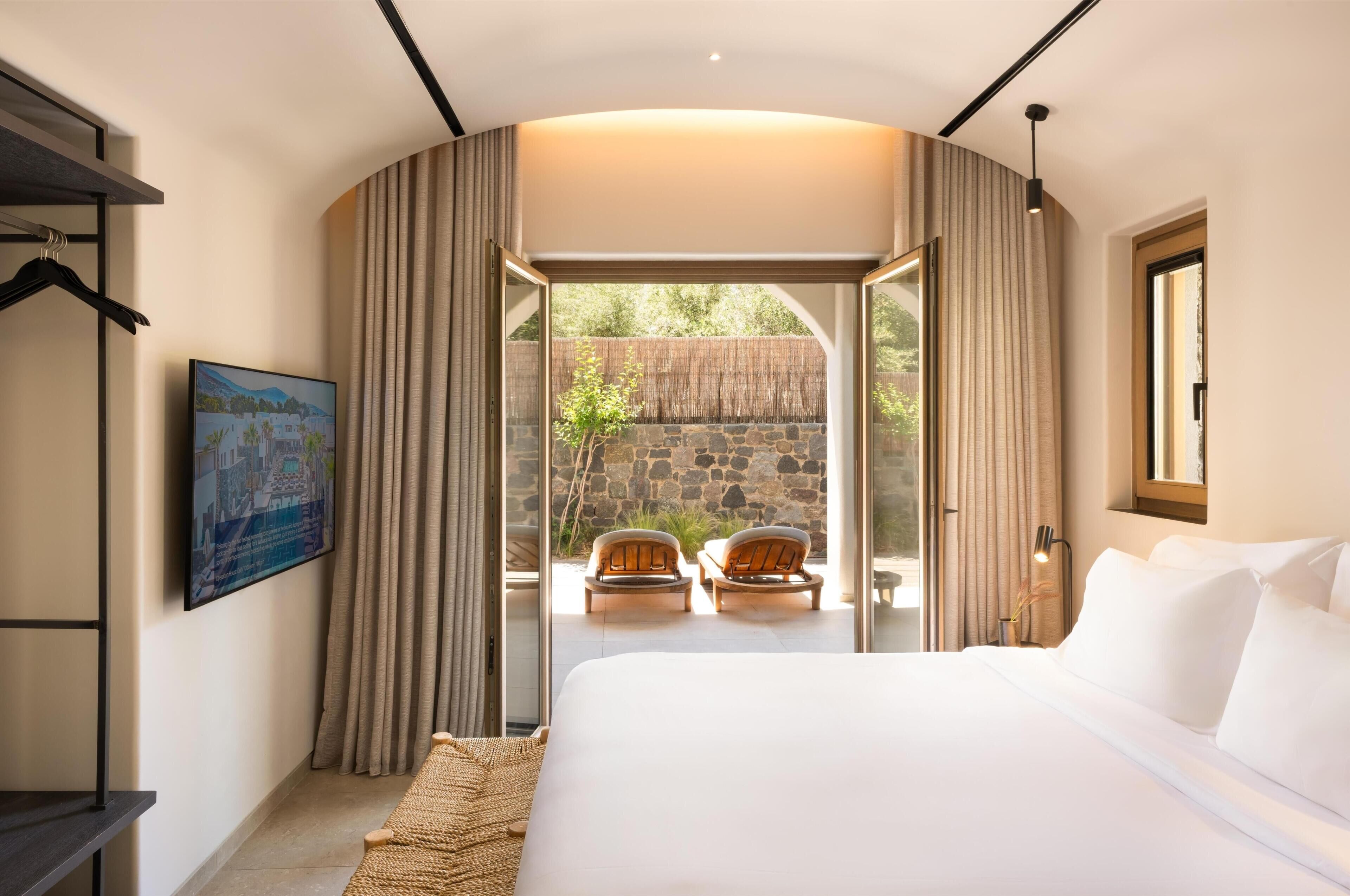 A bedroom with a large bed, a TV, a painting, and a view of the outdoors.