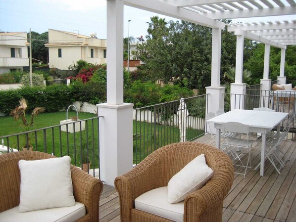 A covered outdoor area with wicker furniture and a white table, surrounded by greenery and a white fence. - Terrazza Vendicari Residence (San Lorenzo)