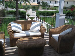 A wicker outdoor seating area with cushions, a wooden deck, and a view of a residential area with buildings and greenery. - Terrazza Vendicari Residence (San Lorenzo)