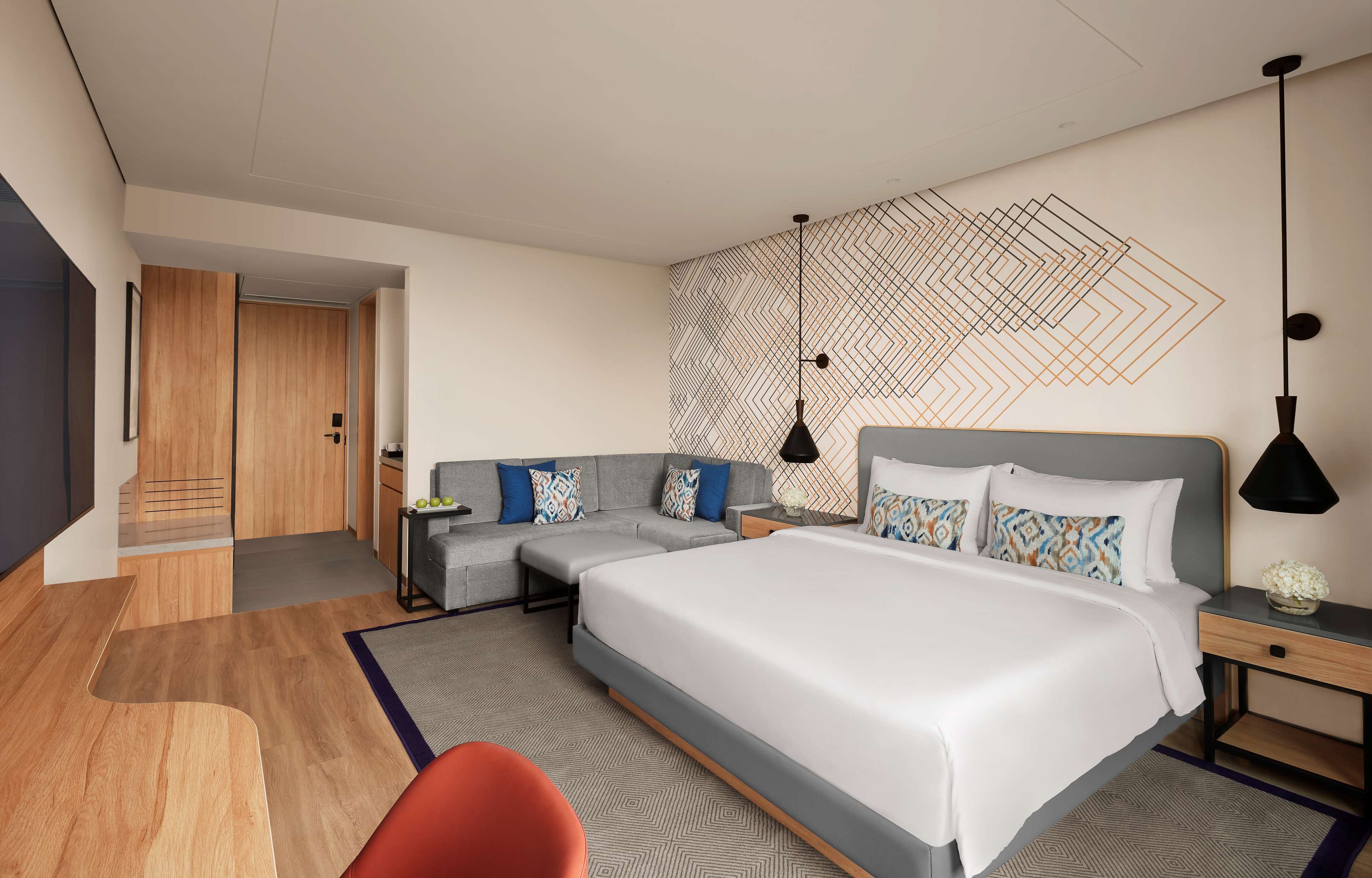A modern hotel room with a large bed, a sofa, a desk, and a small seating area.