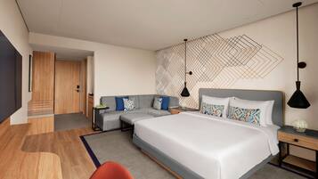 A modern hotel room with a large bed, a sofa, a desk, and a small seating area.
