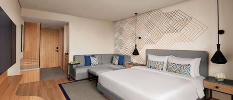 A modern hotel room with a large bed, a sofa, a desk, and a small seating area.