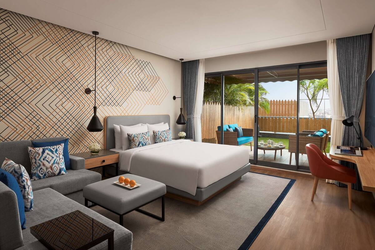 Habitación de hotel moderna con una cama grande, un sofá, un escritorio y un balcón con vistas.