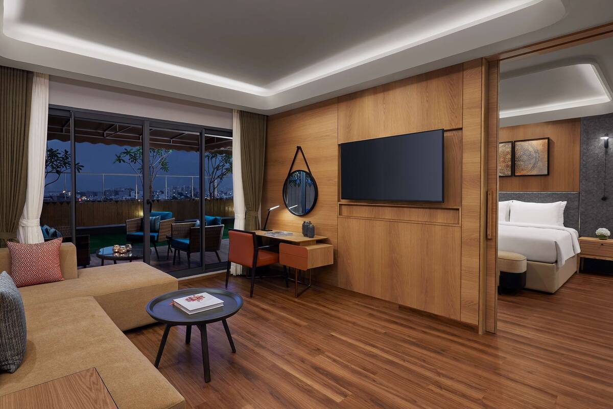 Una habitación de hotel moderna con piso de madera, un sofá, un escritorio, una cama y un televisor grande.