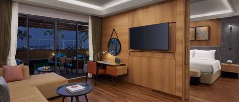 A modern hotel room with a wooden floor, a sofa, a desk, a bed, and a large TV.