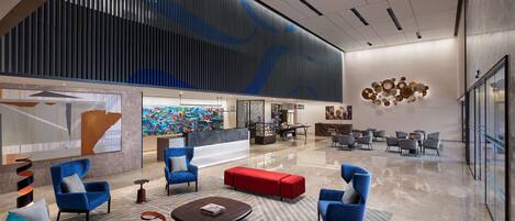 A modern lobby with blue and grey seating, a reception desk, and a large abstract art piece on the wall.
