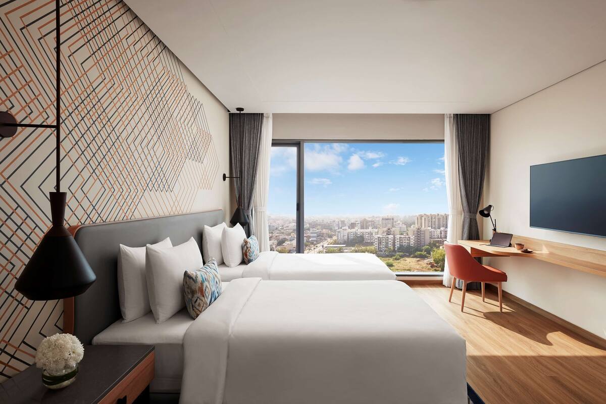 Habitación de hotel moderna con una cama grande, un escritorio con una computadora portátil, un televisor y vista a la ciudad.