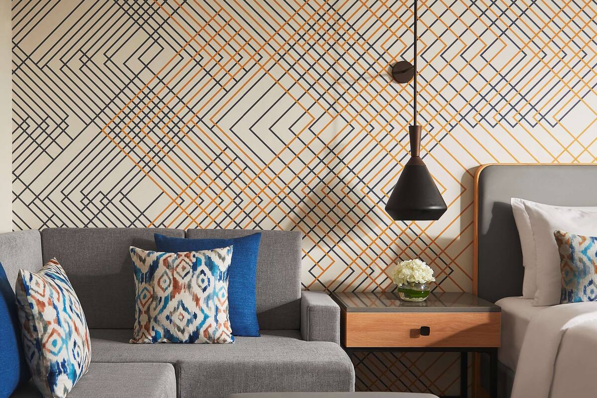 Una habitación de hotel moderna con un sofá gris, una mesita de madera y un sillón gris.