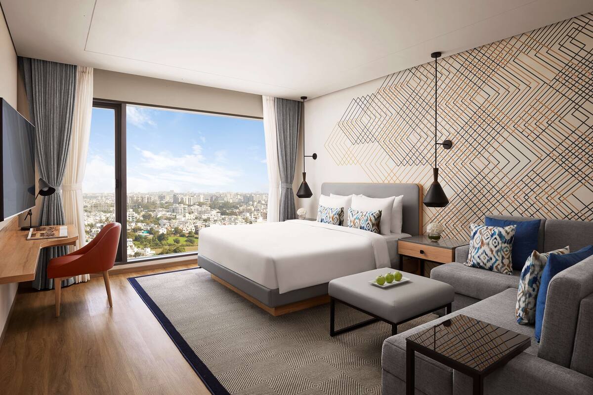 Habitación de hotel moderna con una cama grande, un sofá, un escritorio y vistas a la ciudad.