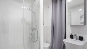 A modern bathroom with a glass-enclosed shower, a white toilet, and a sink with two soap dispensers.