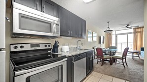 Una cocina equipada con microondas, estufa y lavavajillas. Cuenta con una zona de comedor con mesa y sillas.