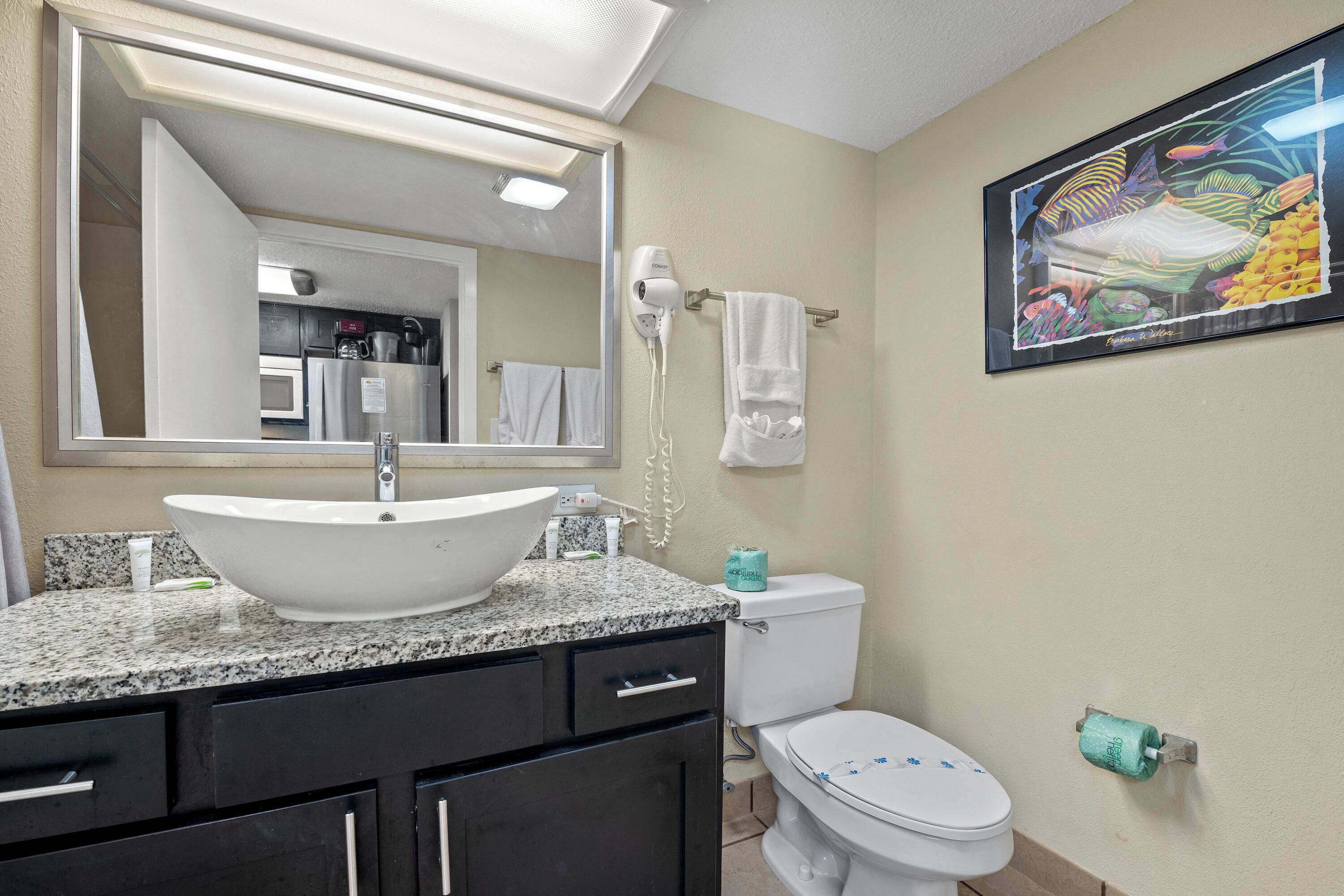 A bathroom with a large mirror, a white sink, a toilet, and a framed painting on the wall.