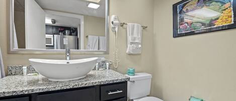 A bathroom with a large mirror, a white sink, a toilet, and a framed painting on the wall.
