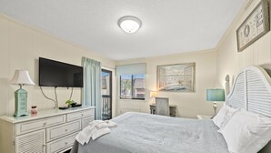 Un dormitorio con cama, cómoda, televisor y ventana con cortinas.
