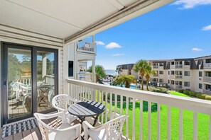 A balcony with a table and chairs, overlooking a pool area and other buildings. - Ocean Forest Villas 215B - Charming 2 Bed/2 Bath Condo in Myrtle Beach (Myrtle Beach)