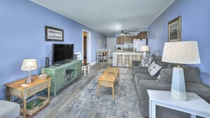 Een woonkamer met een televisie, een groen kastje, een houten salontafel, een witte bijzettafel en een grijze bank.