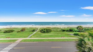 Blick auf die Küste mit Strand, Grünflächen und einer Straße mit Zebrastreifen.