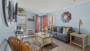 A living room with a sofa, coffee table, and chairs. There is a clock on the wall and a lamp on a side table.