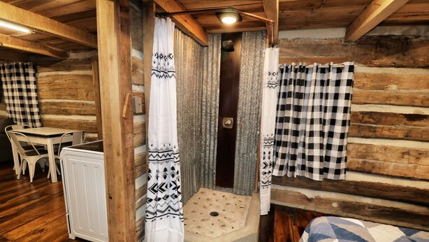 Habitación tipo cabaña de madera con piso de madera, una cama con manta estampada, un radiador blanco, una mesita y una silla.
