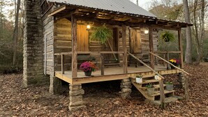 Una cabaña rústica con terraza de madera, base de piedra y plantas colgantes.