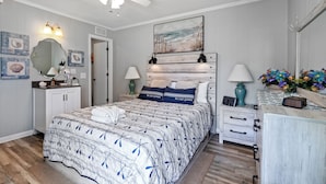 Une chambre à coucher comprenant un lit, des tables de chevet, une commode, un ventilateur de plafond, des lampes fixées au mur et des œuvres d’art.