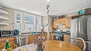 A modern kitchen with a wooden dining table, stainless steel appliances, and a window with blinds. - Next to Boston & Beach, King Beds, Free Parking+EV (Quincy)