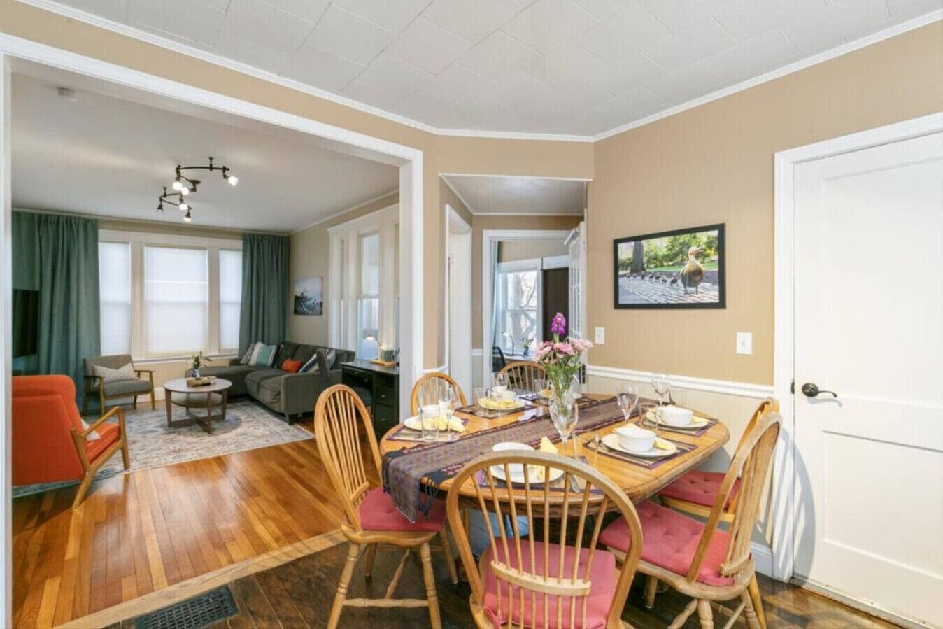 Comedor con una mesa de madera dispuesta para cuatro, rodeado de sillas de madera con cojines rosados.
