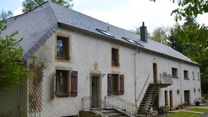 Un edificio a due piani con fondamenta in pietra, una scala che conduce all'ingresso e un piccolo balcone al secondo piano.