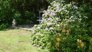 Un giardino con una struttura in pietra, circondato da vegetazione rigogliosa e piante fiorite.