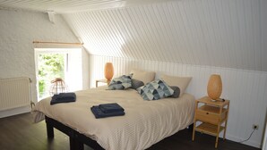 Una camera da letto con soffitto spiovente, un letto con copripiumino color beige, due comodini con lampade e una finestra vista verde.