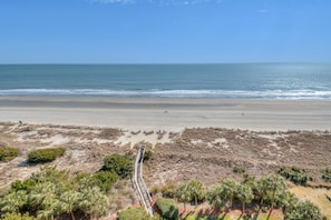 Uma praia com calçadas que levam à água, cercada por vegetação seca e palmeiras.