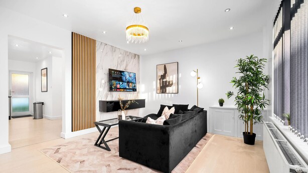 A modern living room with a black sofa, a wooden accent wall, a TV, and a chandelier. - 3bed house, in close proximity to the centre suitable for 6 guests!Pet-Friendly! (West Midlands)