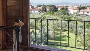 Ein Zimmer mit einem großen Bogenfenster, das Blick auf eine grüne Landschaft und entfernte Gebäude gewährt.