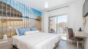 A bedroom with a large bed, a desk, and a chair. There is a view of buildings through a glass door. - Emerald Apartment, AC, Swimming Pool !new! (Portimão)
