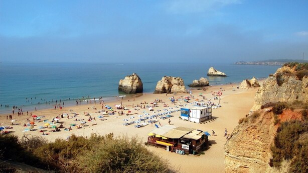 A beach with large rock formations, a sandy shore, and a small building with a sign. - Emerald Apartment, AC, Swimming Pool !new! (Portimão)
