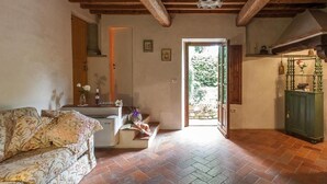 Un ambiente accogliente con un divano, un tavolino con fiori, una scala e una porta che dà sull'esterno.