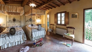 Una stanza con soffitto in legno, un letto a baldacchino, una finestra vista verde e una sedia con un tavolo.