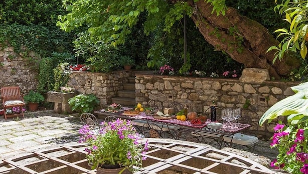 Patio esterno con pareti in pietra, tavolo apparecchiato per mangiare e piante in vaso.