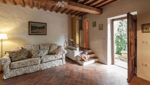 Un accogliente soggiorno con divano, lampada, una scala che conduce a una zona esterna e un soffitto in legno rustico.