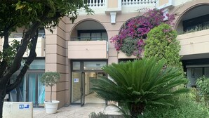 Ein Gebäude mit einem zentralen Eingang, umgeben von einem Garten mit verschiedenen Pflanzen und einer Palme.