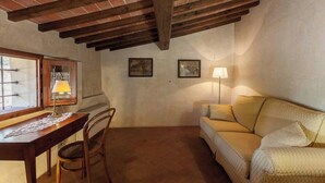 A cozy room with a wooden desk, chair, and a yellow sofa. There are two framed pictures on the wall and a lamp on the sofa. - Lovely Apartment with private patio and garden (Comune di Sesto Fiorentino)