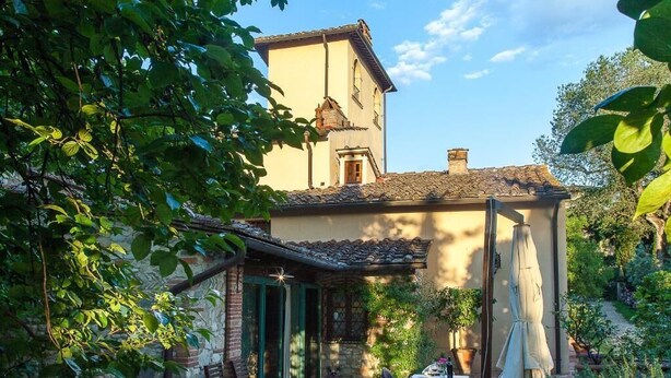 A rustic building with a stone facade, a tiled roof, and a small balcony with a table and chairs. - Lovely Apartment with private patio and garden (Comune di Sesto Fiorentino)