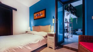 A bedroom with a bed, a nightstand, a wall-mounted painting, and a sliding glass door leading to a balcony with outdoor furniture.