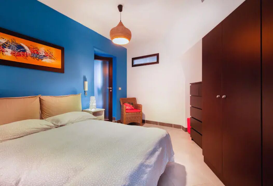 A bedroom with a bed, a wardrobe, a chair, and a painting on the wall.