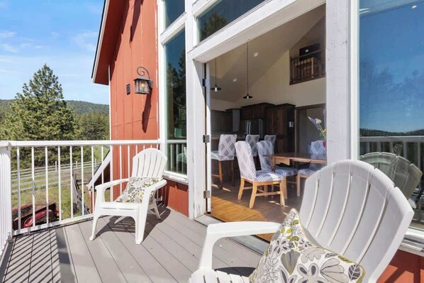 Una terraza de madera con sillas blancas y una zona de comedor con sillas estampadas.