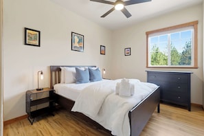 Un dormitorio con cama, mesitas de noche, cómoda y ventana con vista a árboles.