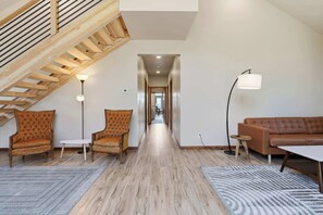 A spacious living area with a high ceiling, a wooden staircase, and a view into the hallway.