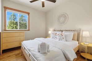 A bedroom with a bed, a dresser, a window with a view of trees, a ceiling fan, and a decorative wall piece.