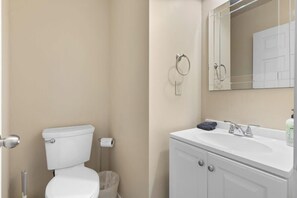 Un baño con inodoro, lavamanos, espejo y cubo de basura.